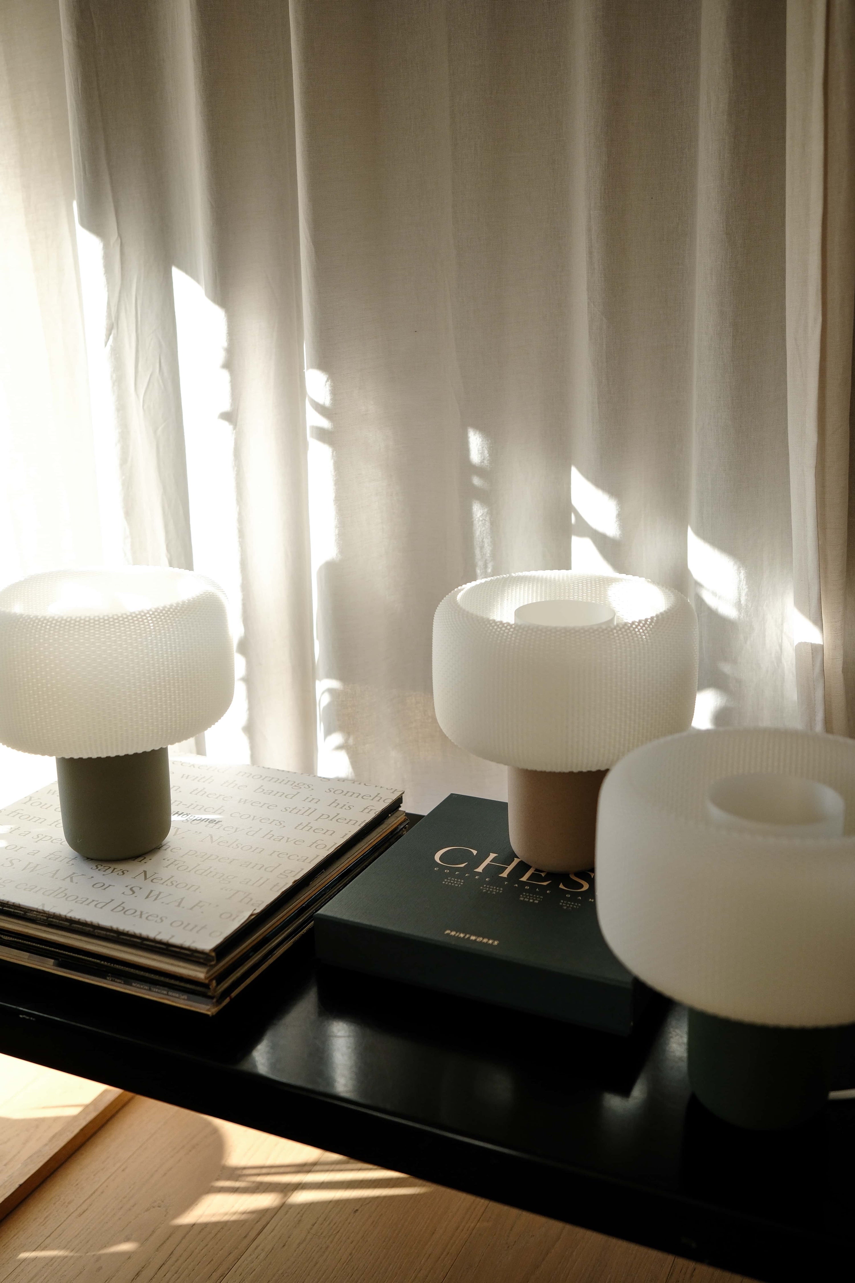 Three white table lamps on a dark surface with a blurred curtain background