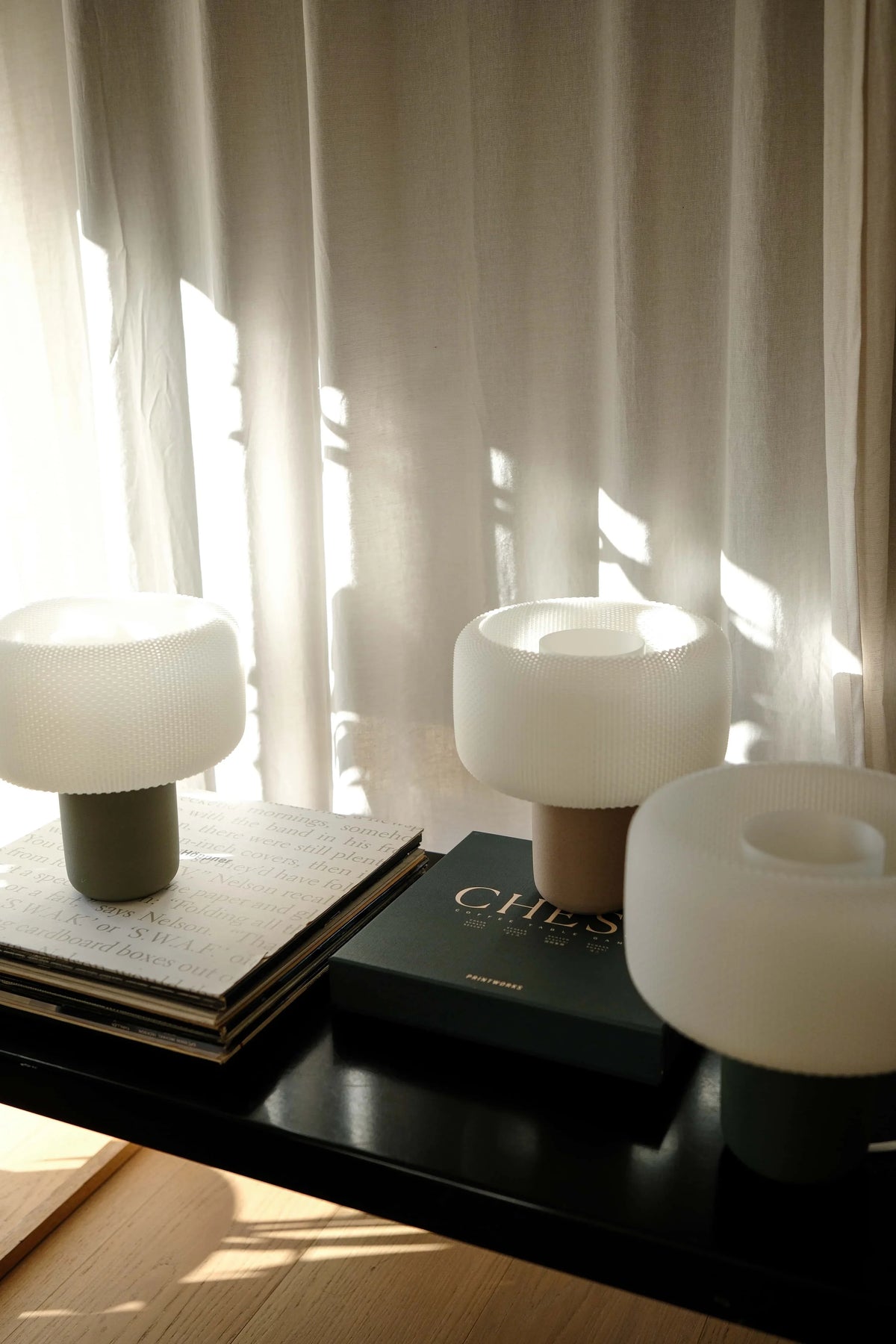 Three white table lamps on a dark surface with a blurred curtain background