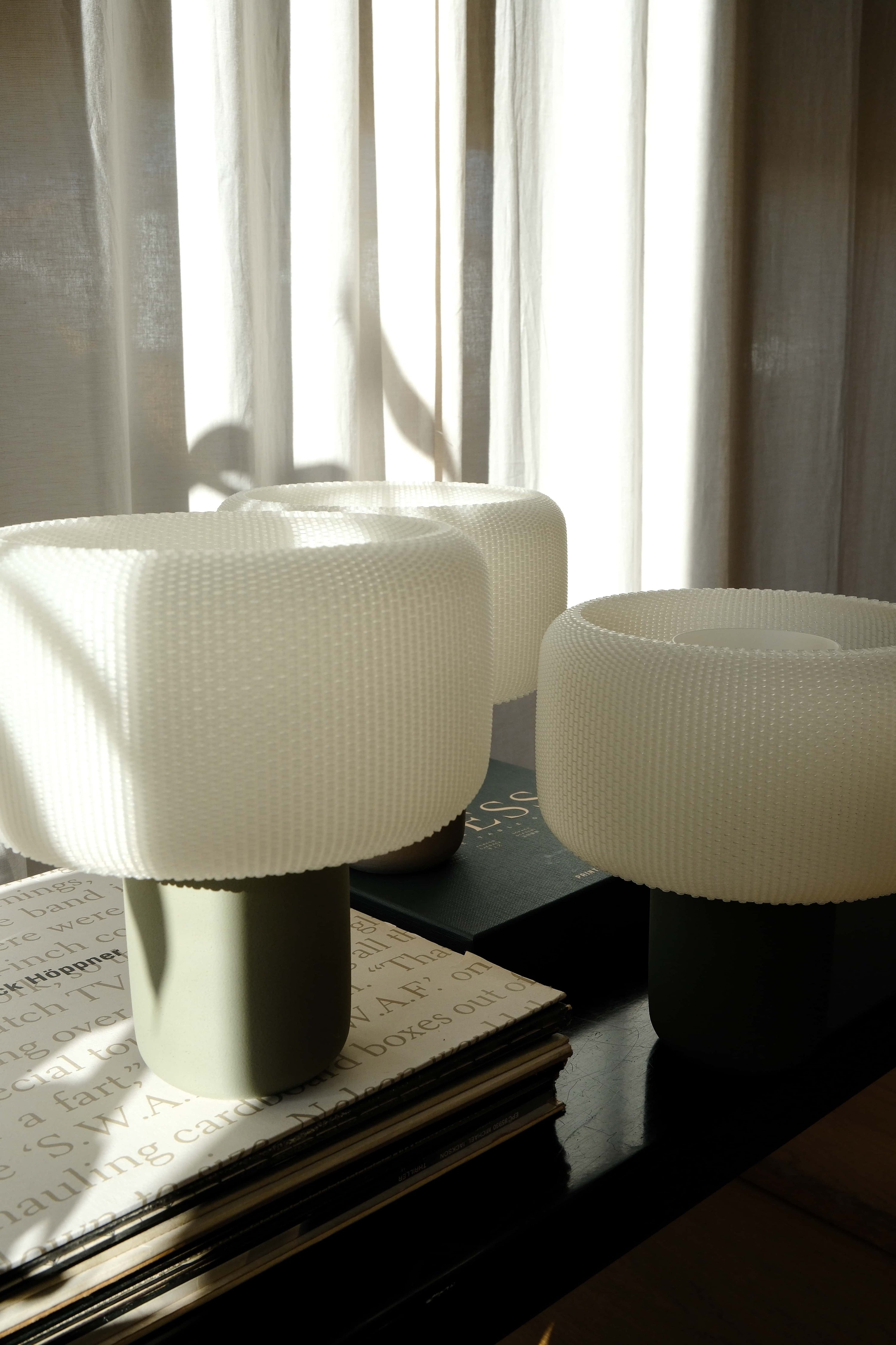 Three white textured stools on a dark surface with light filtering through curtains in the background.