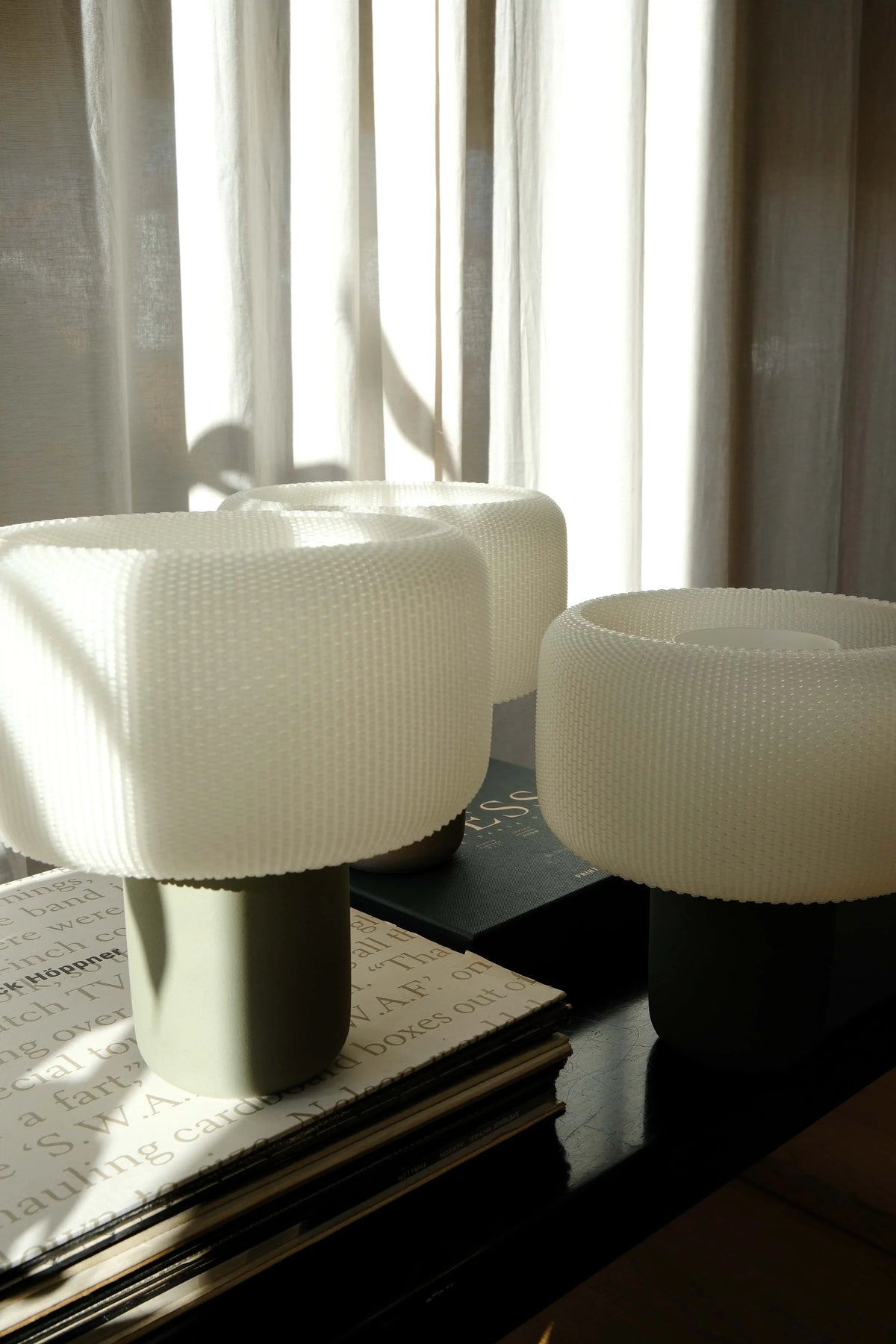 Three white textured stools on a dark surface with light filtering through curtains in the background.