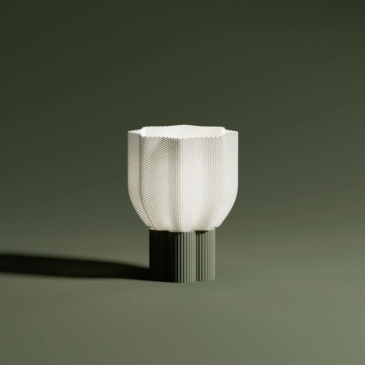Bloom lamp lit with pleated beige base on olive green background. Warm glow and contemporary mood.