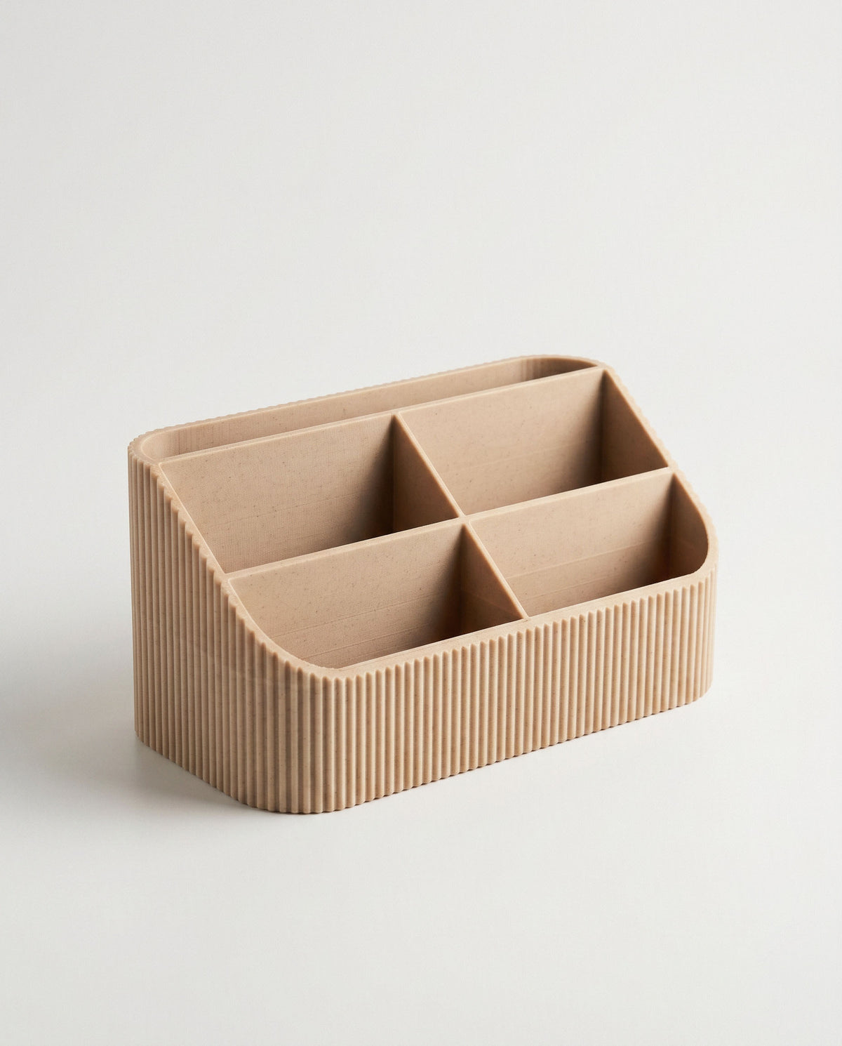 An elevated, three-quarter angled photograph of the empty COCO fluted desk organizer against a clean off-white background, revealing its depth and side profile. This view clearly shows the layout of the five varied compartments and the textured ribbed pattern wrapping around the form.