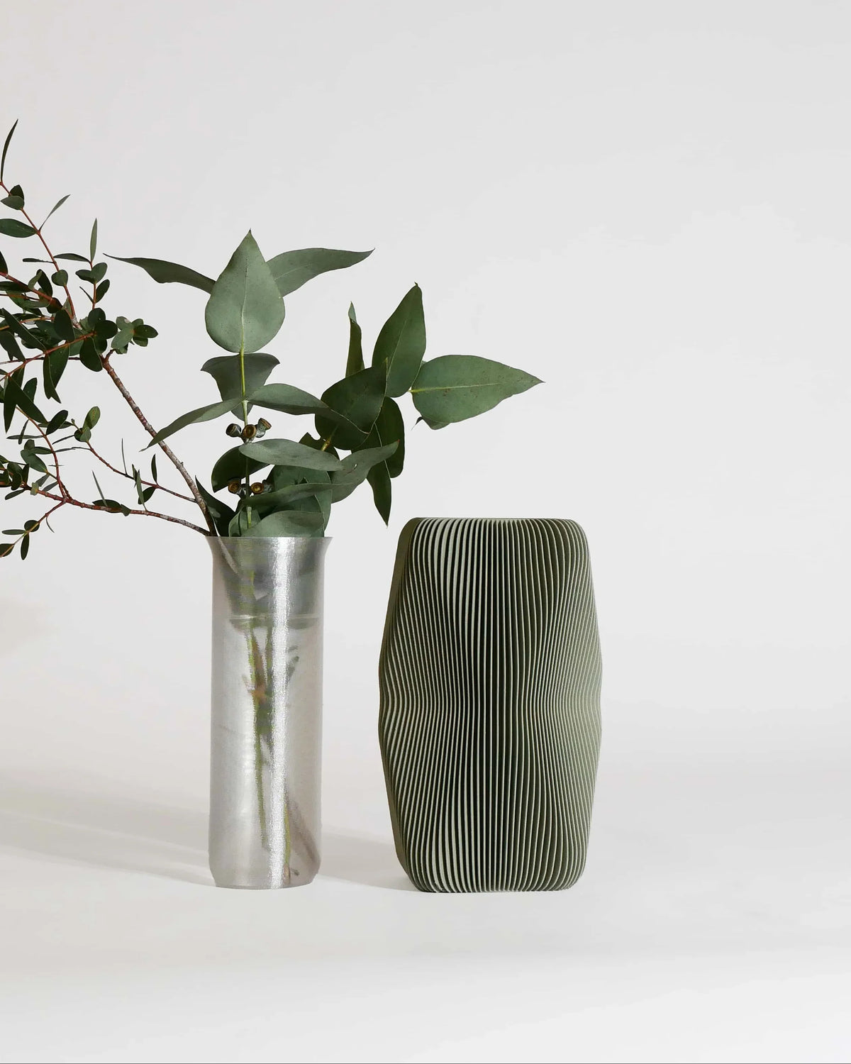 SOHO Olive vase beside silver cylinder vase, fresh botanicals, grey-green matte, interior styling