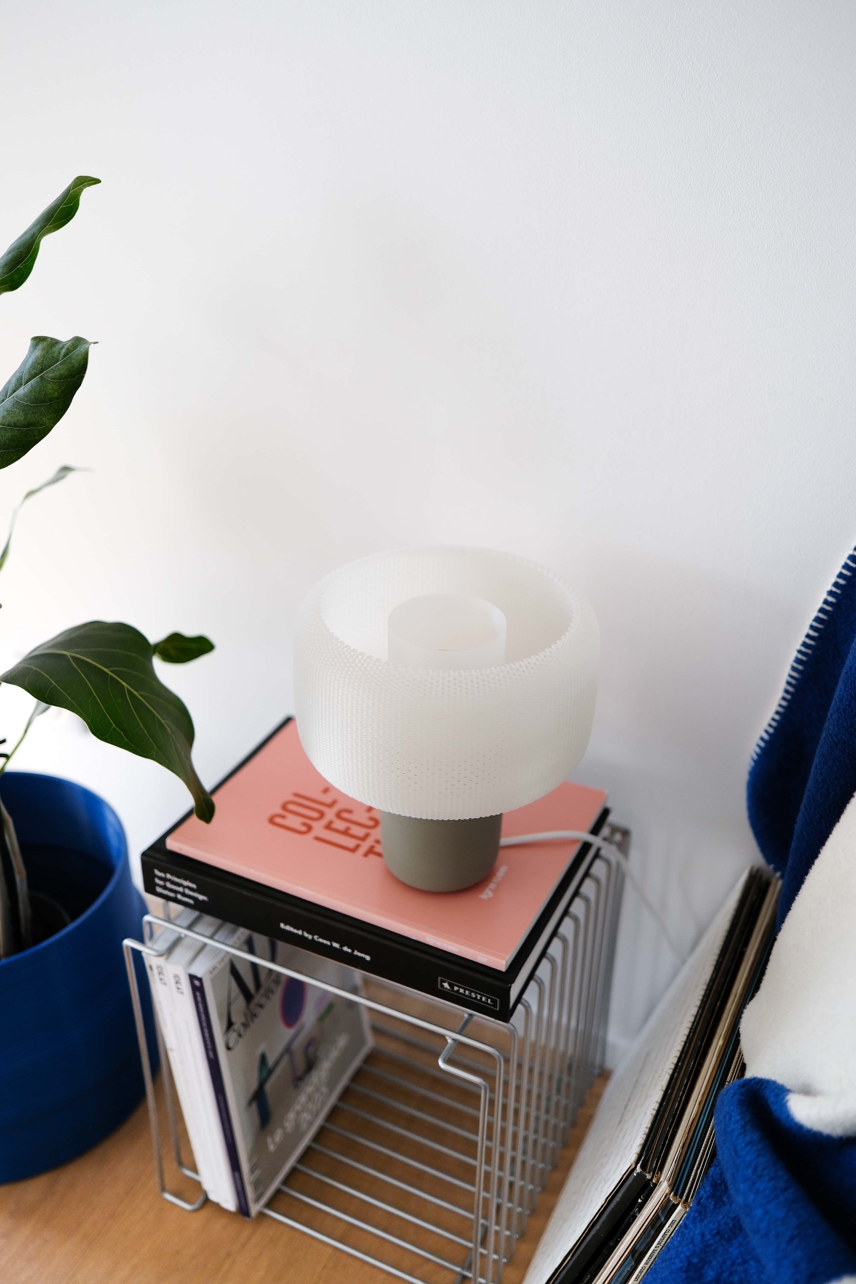 Lamp on a stack of books with a plant and blue chair in the background #color_olive