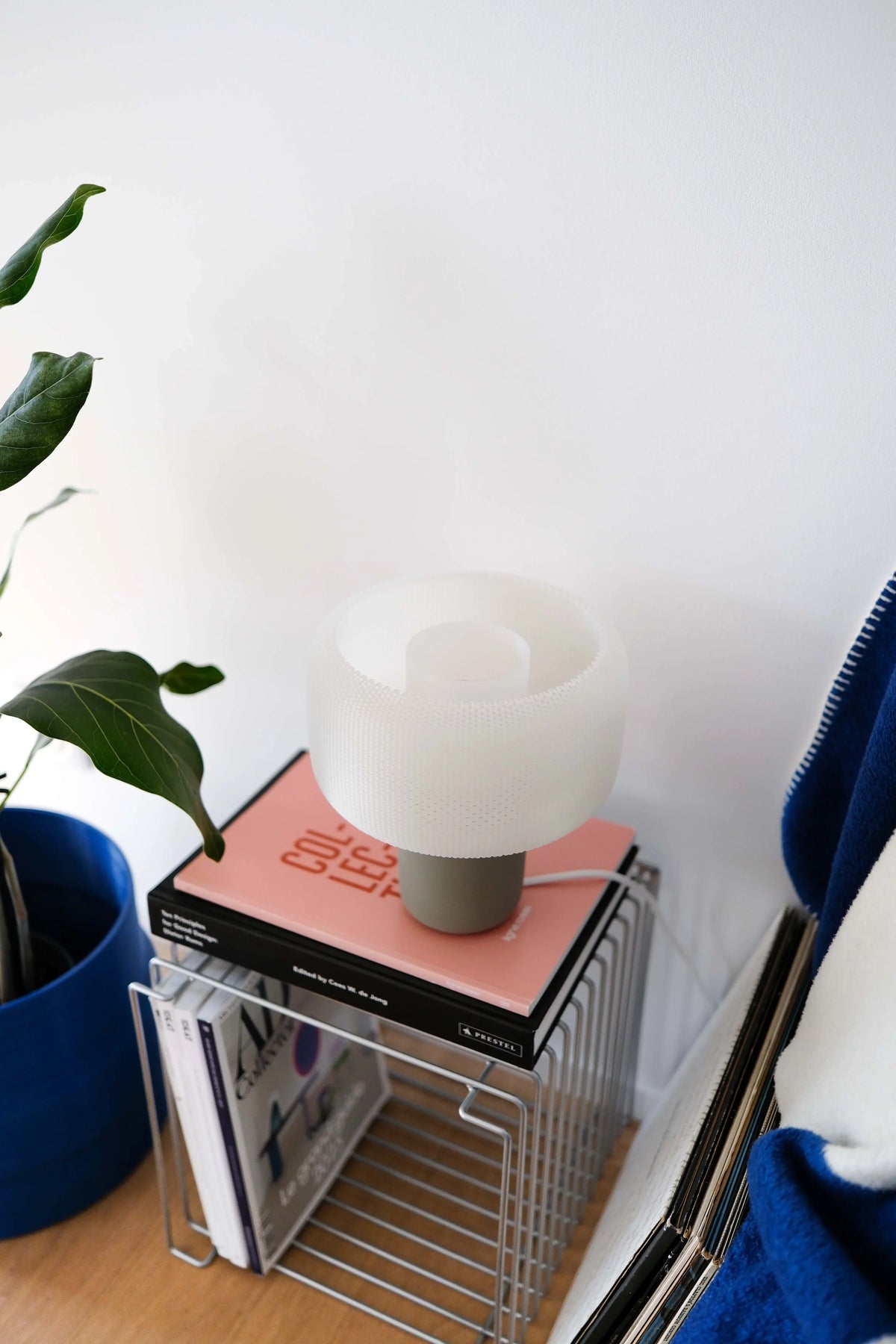 Lamp on a stack of books with a plant and blue chair in the background #color_olive