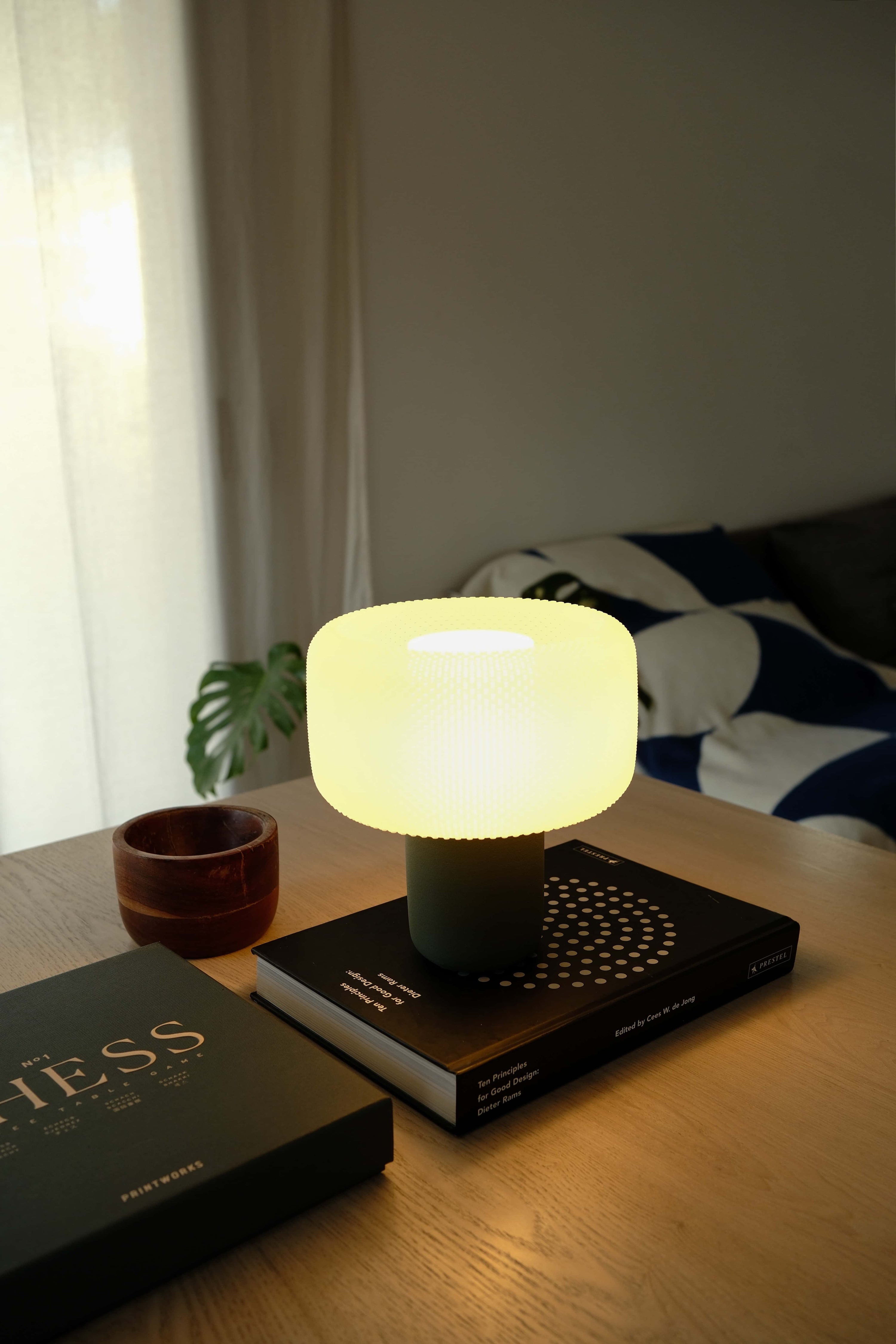 Futuristic light bulb on a table with books and a plant in a softly lit room. #color_green