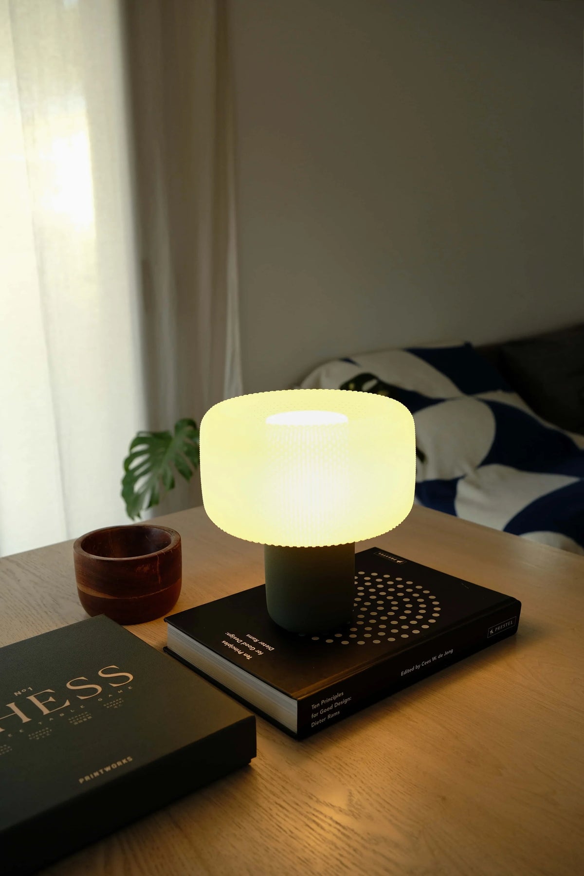 Futuristic light bulb on a table with books and a plant in a softly lit room. #color_green