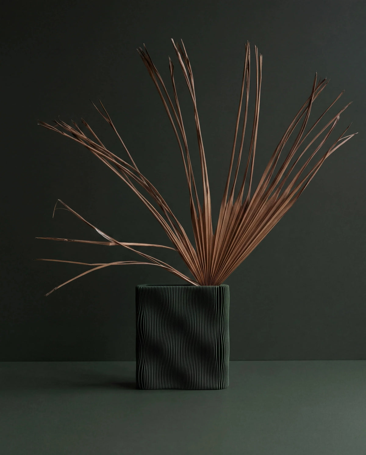 TIDE sculptural vase Green with dried palm stems, forest green matte finish, wave-ribbed bio-sourced wood