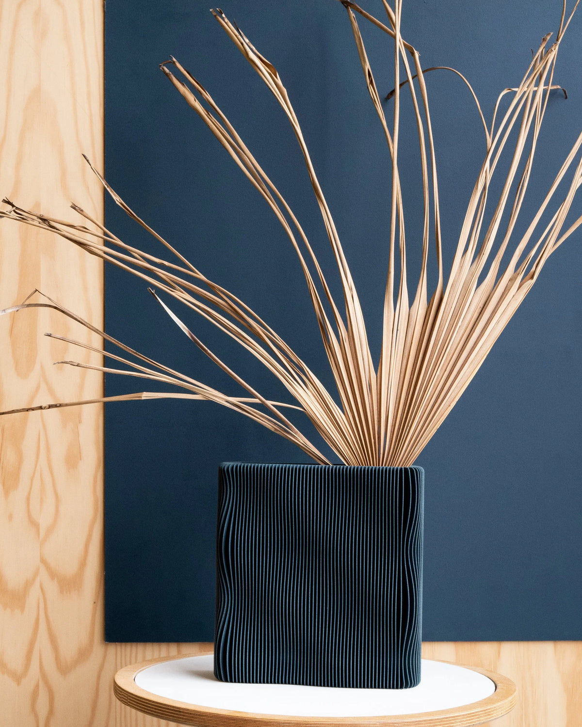 TIDE sculptural vase Blue with dried palm stems, deep navy matte finish, wave-ribbed bio-sourced wood, 22cm