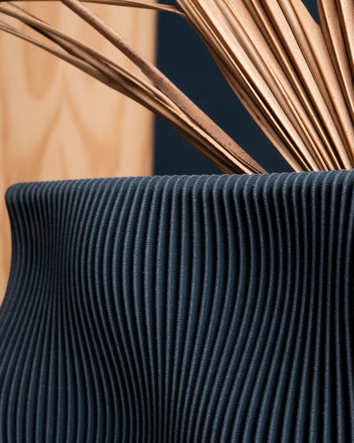 TIDE vase Blue extreme close-up wave-ribbed texture, deep navy matte bio-sourced wood composite finish