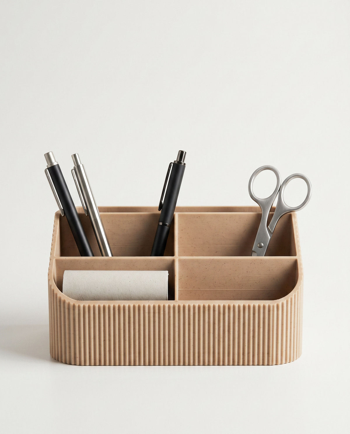 A clean, front-facing portrait of the COCO fluted wood desk organizer against a seamless off-white background. The compartments are neatly filled with three varied pens, a pair of polished metal scissors, and a small textured paper roll, highlighting its rhythmic ribbed texture.