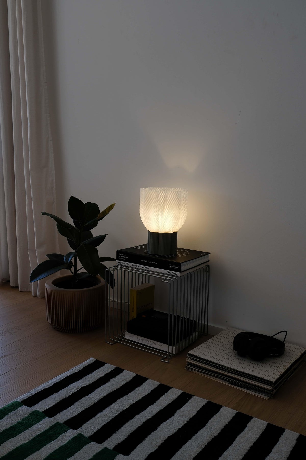 Bllom Lamp on a side table next to a plant and books in a dimly lit room.
