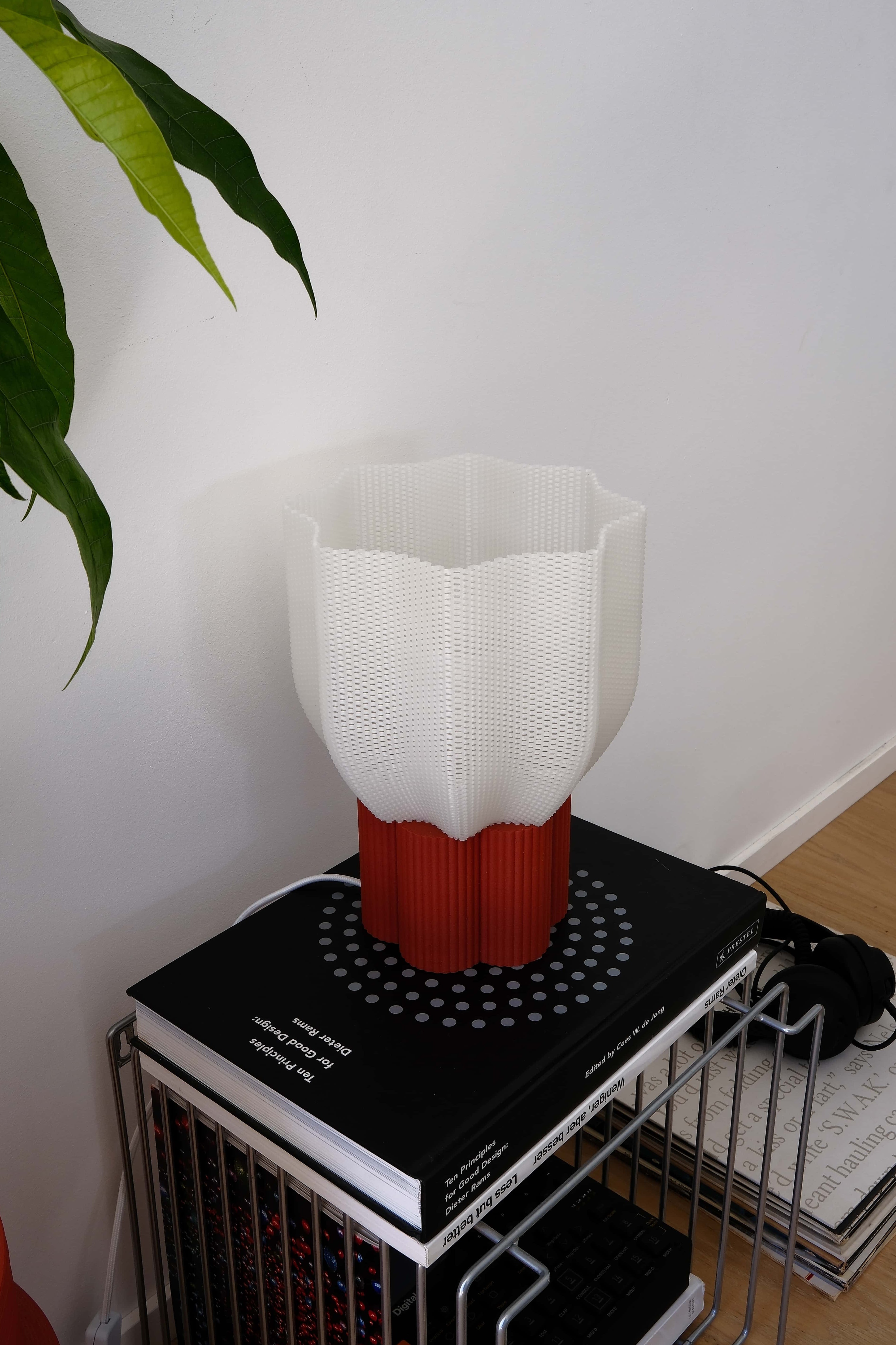 White and red lamp on a black book with a plant in the corner