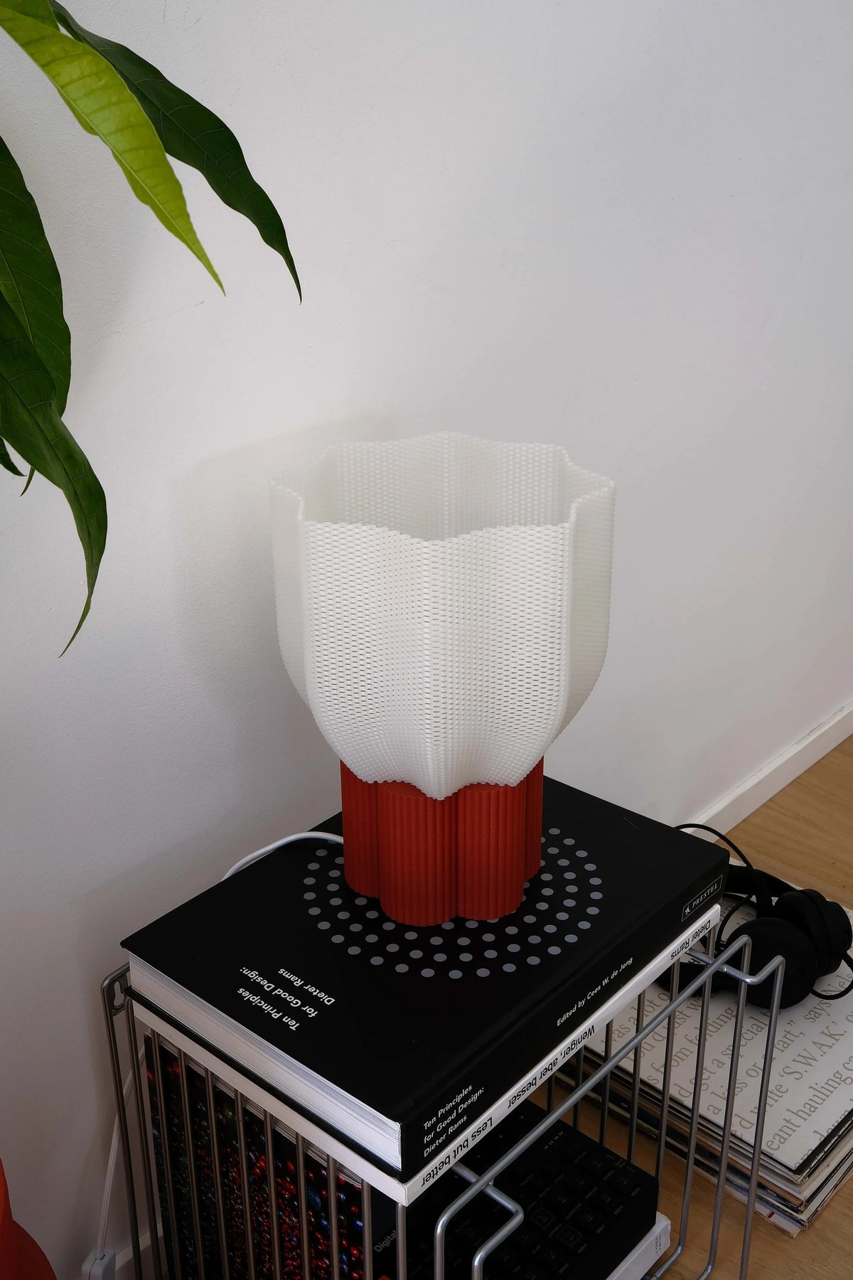 White and red lamp on a black book with a plant in the corner