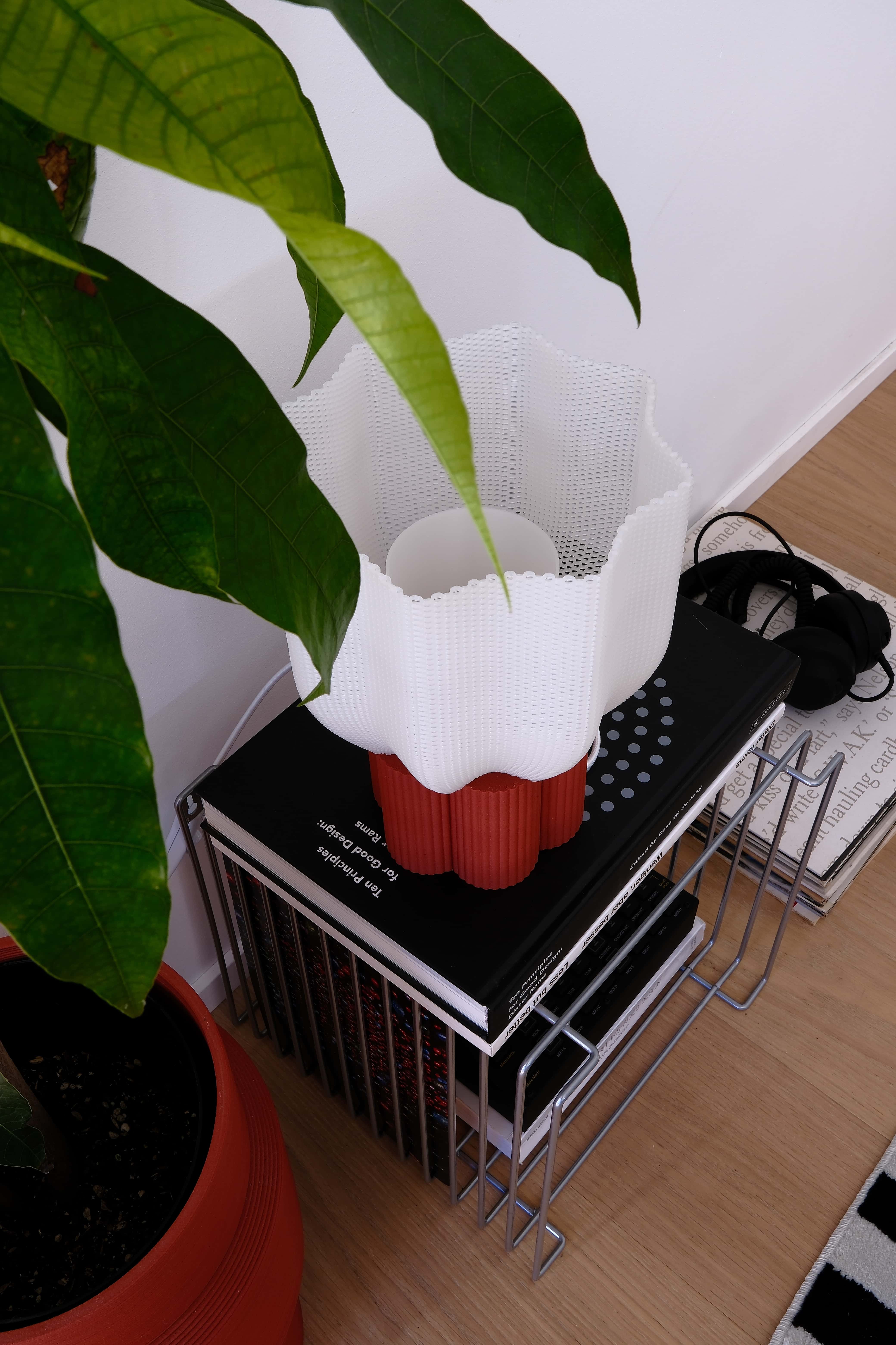 Small white lamp with red base on a black stand next to a plant