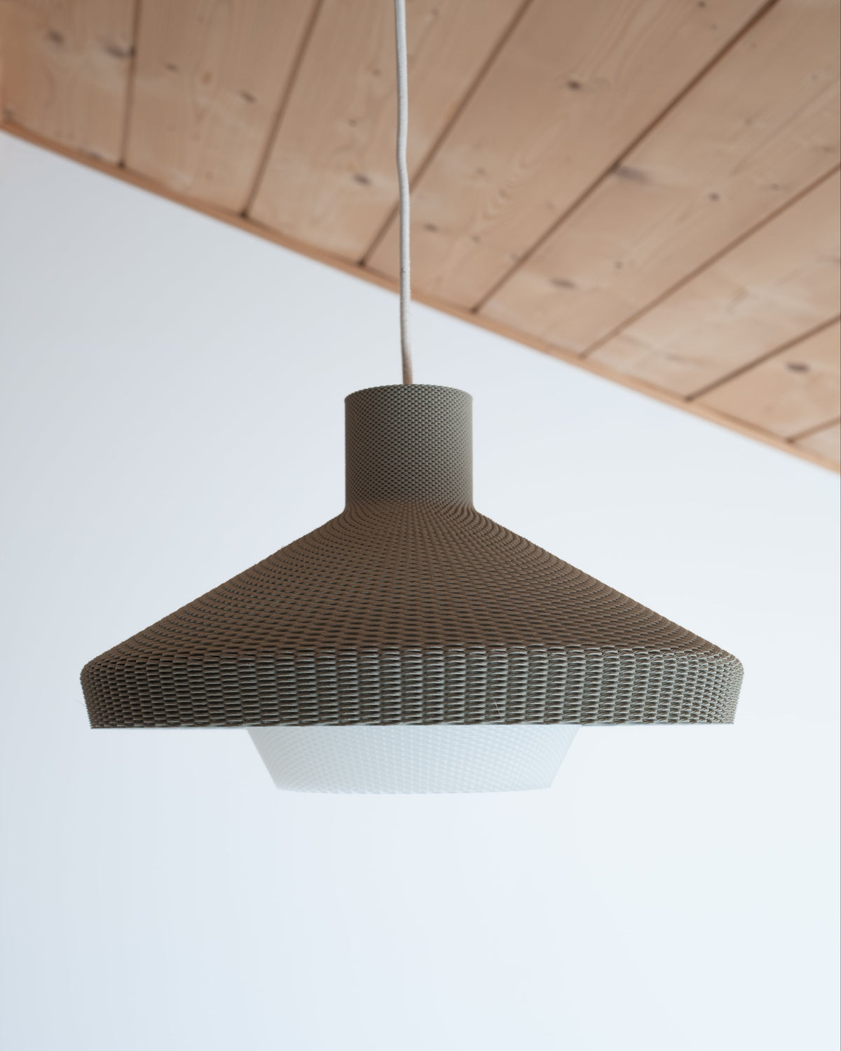 Pendant light with woven design hanging from a wooden ceiling.