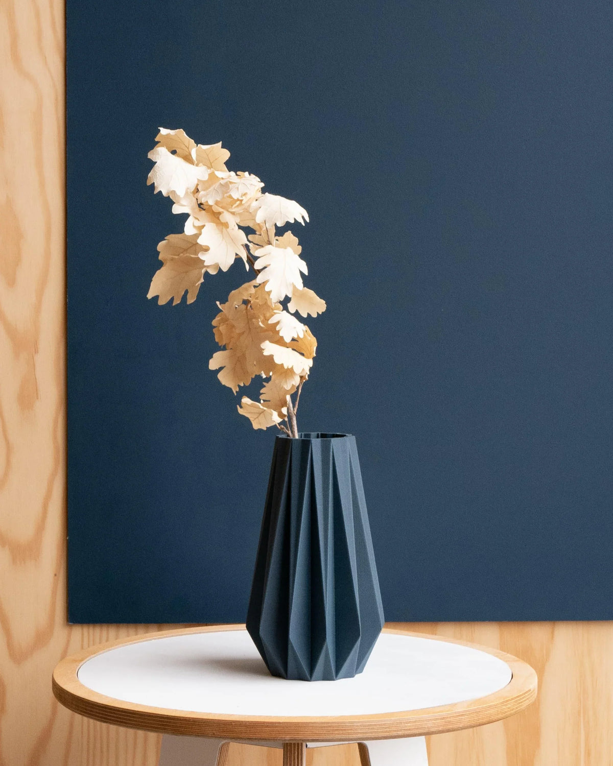 Blue Origami Vase 20cm with dried stem against a blue wall