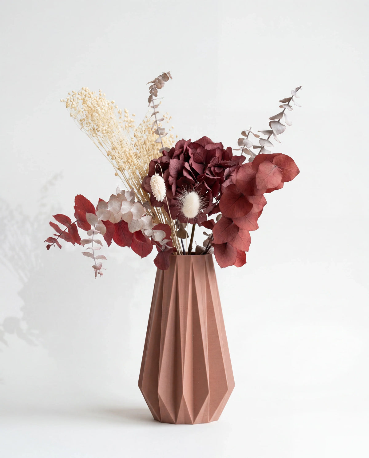 Terracotta origami vase with dried flowers arrangement - minimalist design white background
