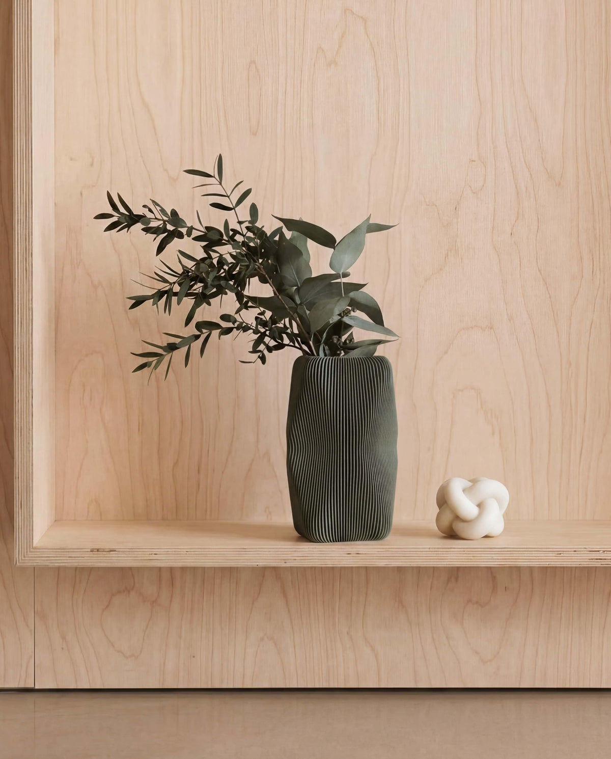 Vase with greenery on a wooden shelf against a light wood panel background