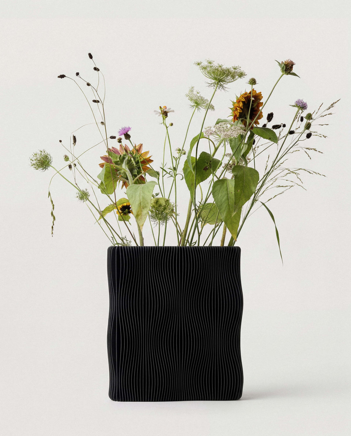 TIDE vase Black with sunflowers and wildflowers front view, fine ribbed texture, matte black, white background