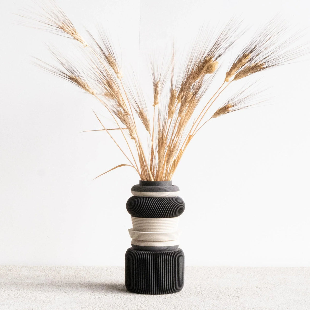 A full view of the NU modular vase in dark grey, styled with dried flowers. Its clean silhouette and deep color bring a bold yet subtle accent to any modern interior.