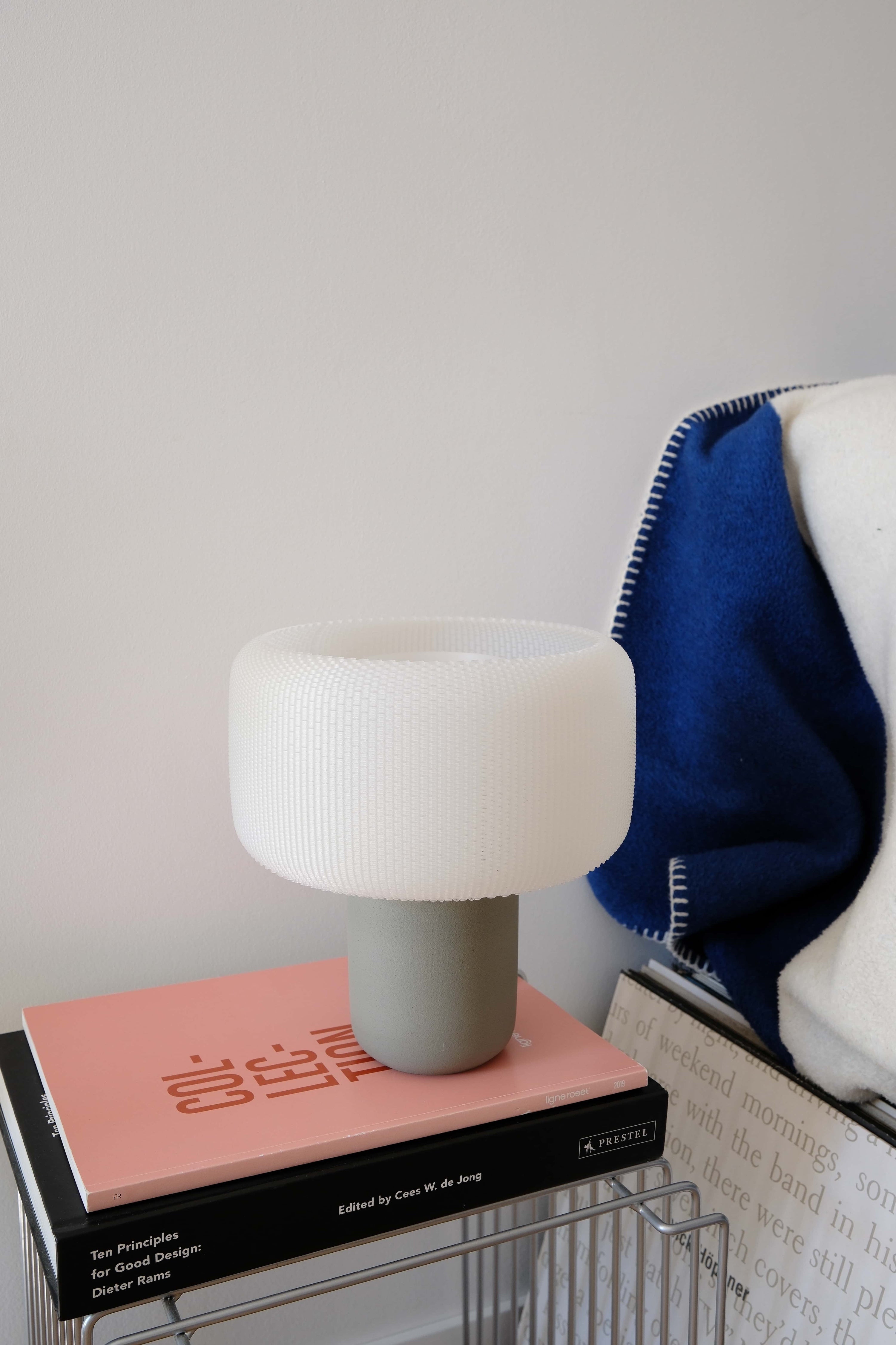 White lamp on a stack of books with a blanket in the background #color_olive