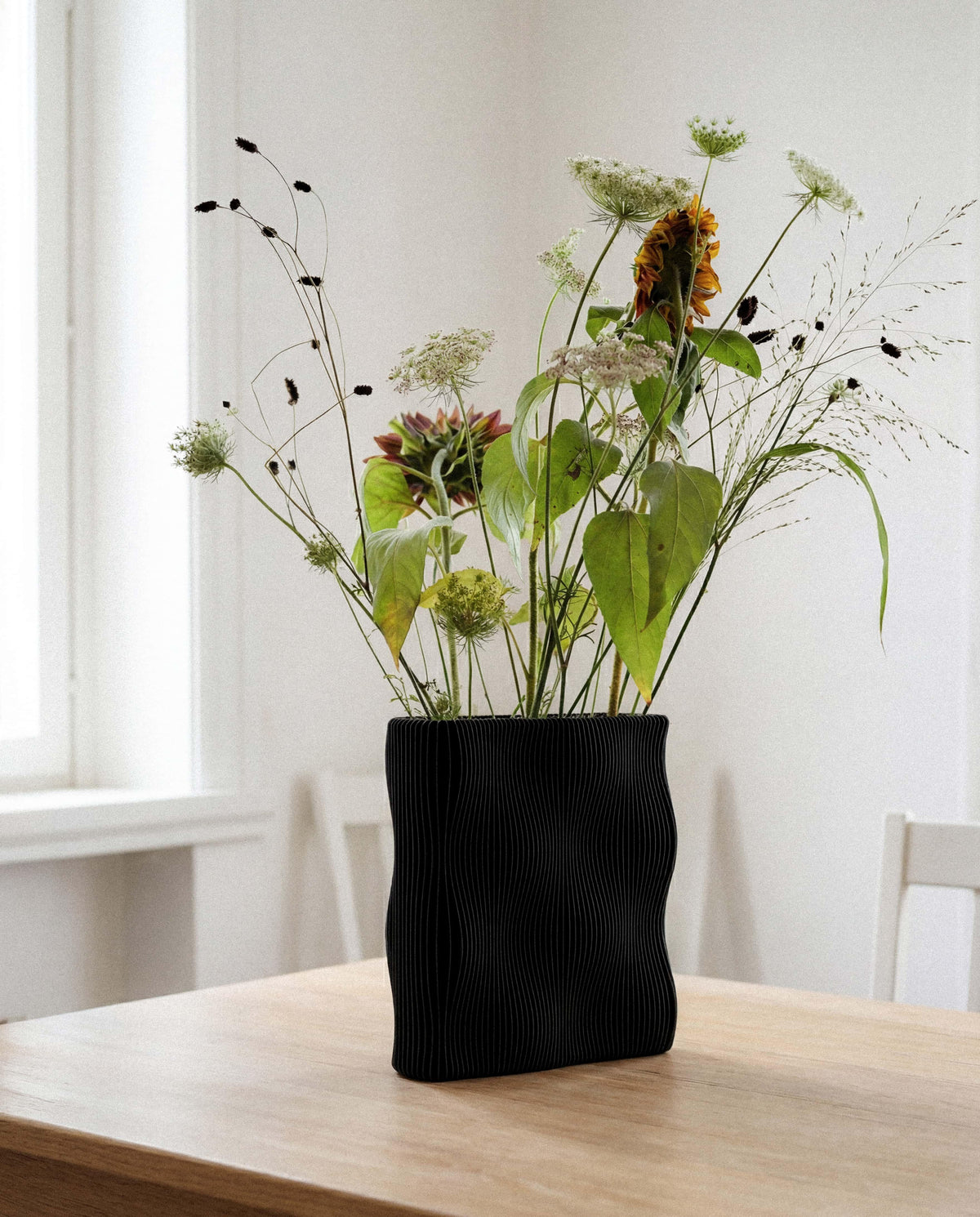 TIDE Black sculptural vase with wildflowers on wooden table, interior lifestyle, wave-ribbed organic form