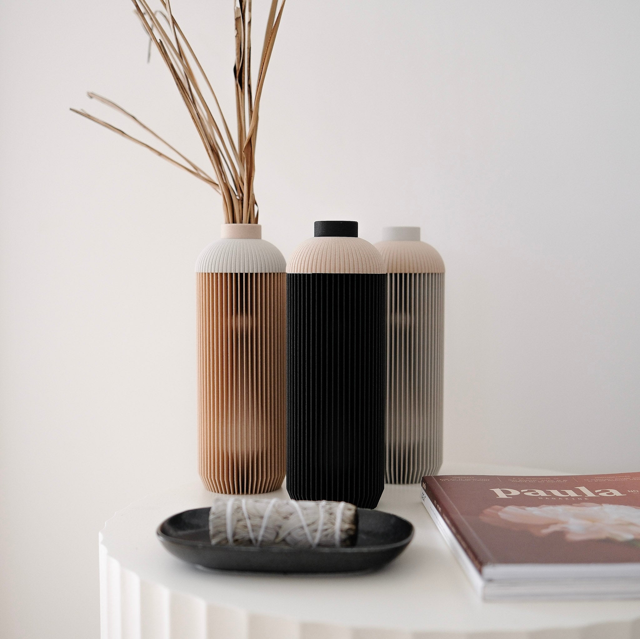 Three decorative vases on a white surface with a book