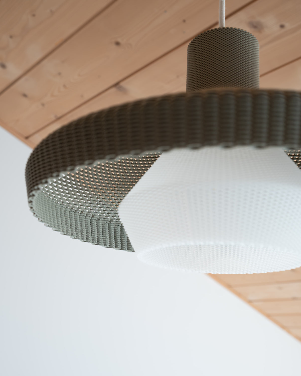 Close-up of a modern pendant light with a textured design on a wooden ceiling.