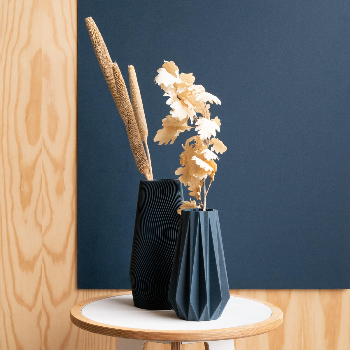 Origami petrol blue vase and wave petrole blue vase with dried flowers stems against a blue wall decor