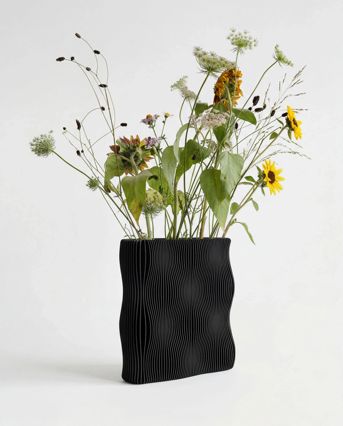 TIDE sculptural vase Black with sunflowers and wildflowers, wave-ribbed matte black bio-sourced wood, 22cm