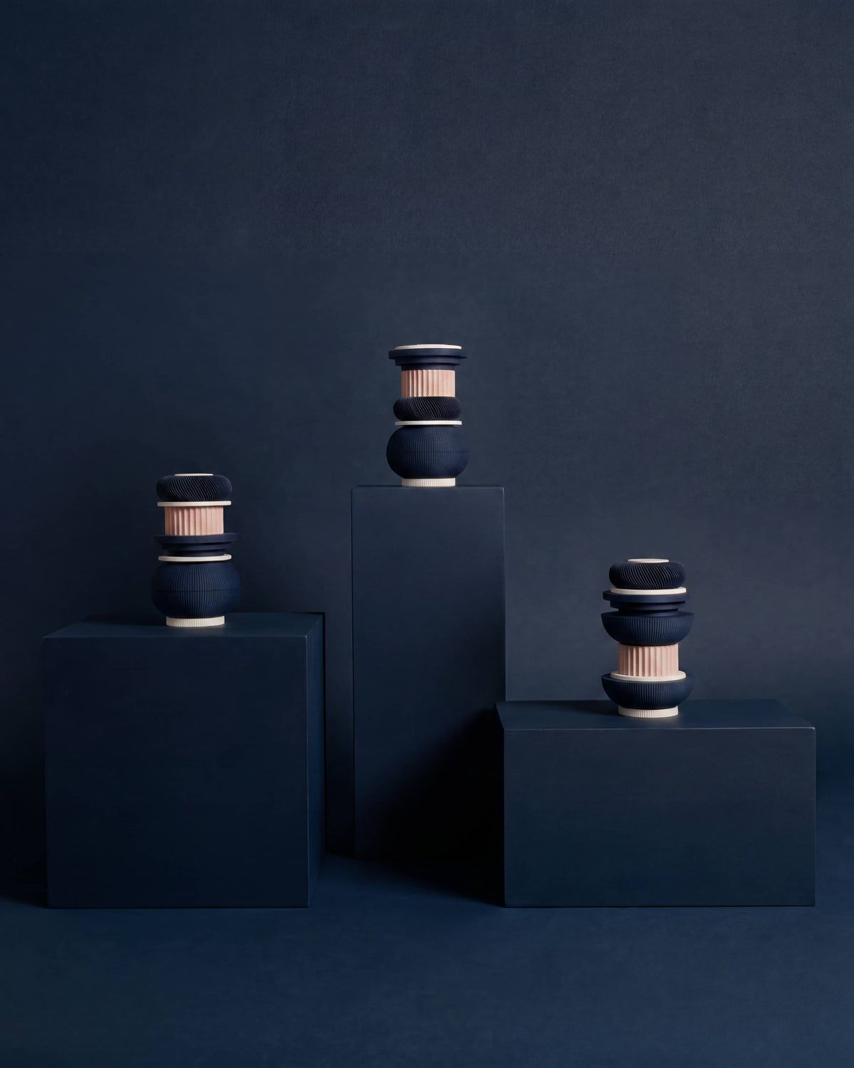 Minimum Design TOTEM modular vase, three cobalt blue and blush pink configurations displayed on geometric plinths, dark blue editorial setting